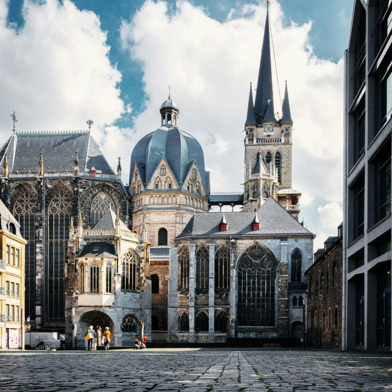 Historisches Kirchengebäude mit markanten Türmen und großer Kuppel, aufgenommen auf einem offenen Platz bei blauem Himmel.